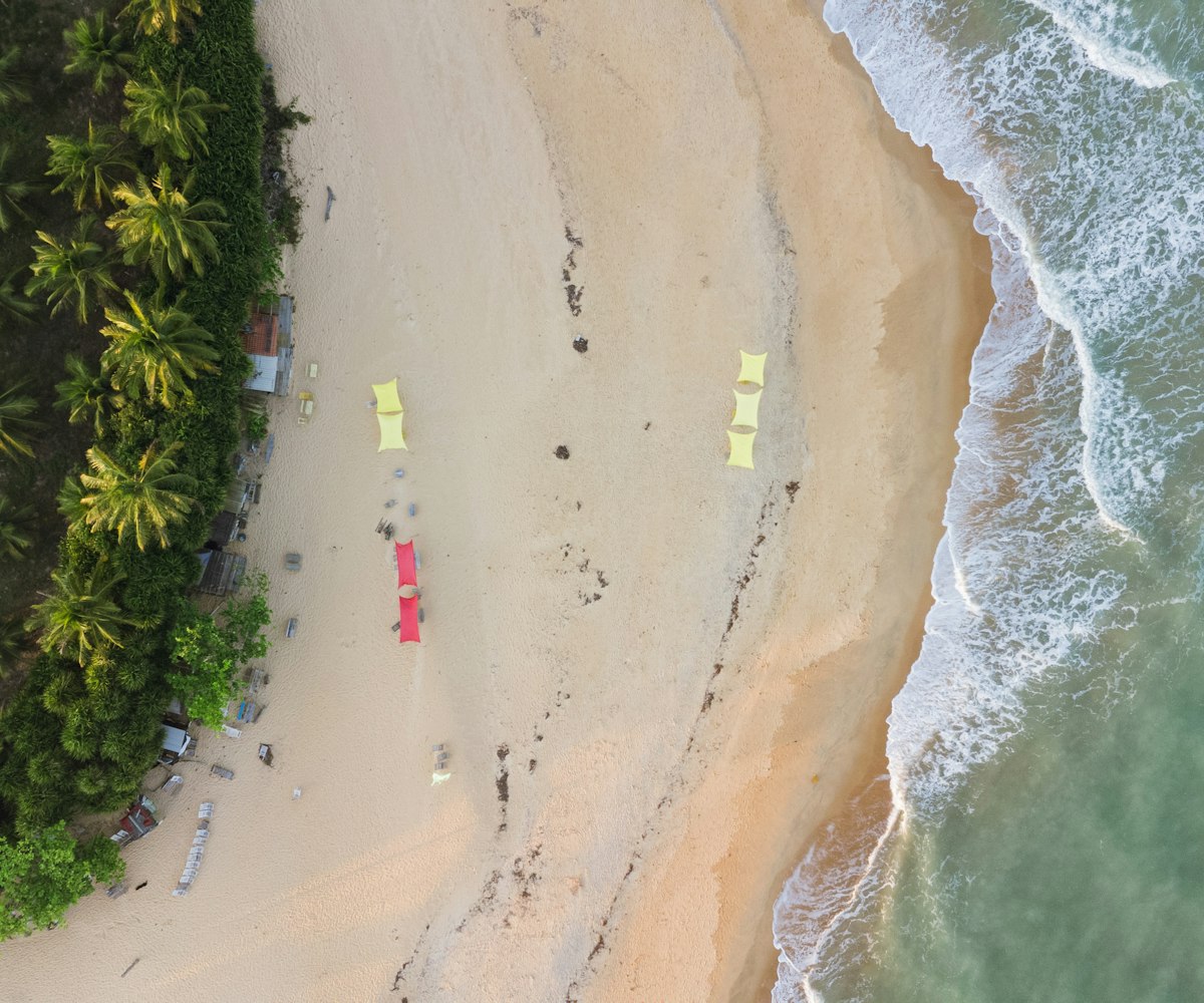 Vista aérea de praia com coqueiral, areia clara e barracas no litoral sul da Bahia